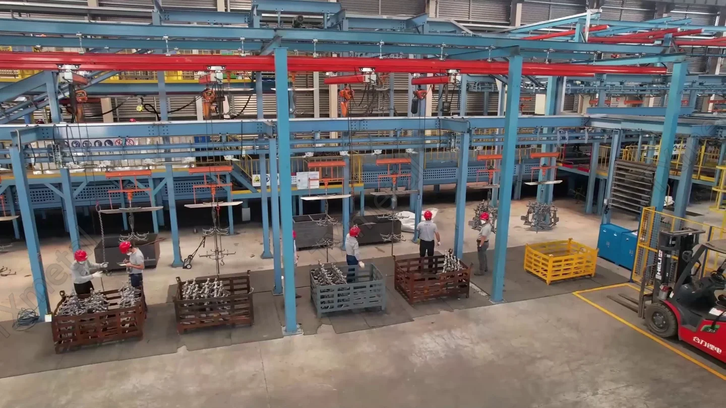 Overhead monorail conveyor system with workers handling castings in TXmetal foundry workshop.
